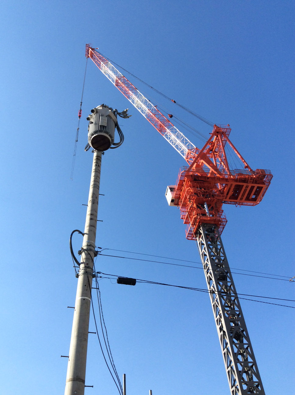 silhouetted against a clear blue sky, an orange and shiny metal crane and a silver-grey communications mast.